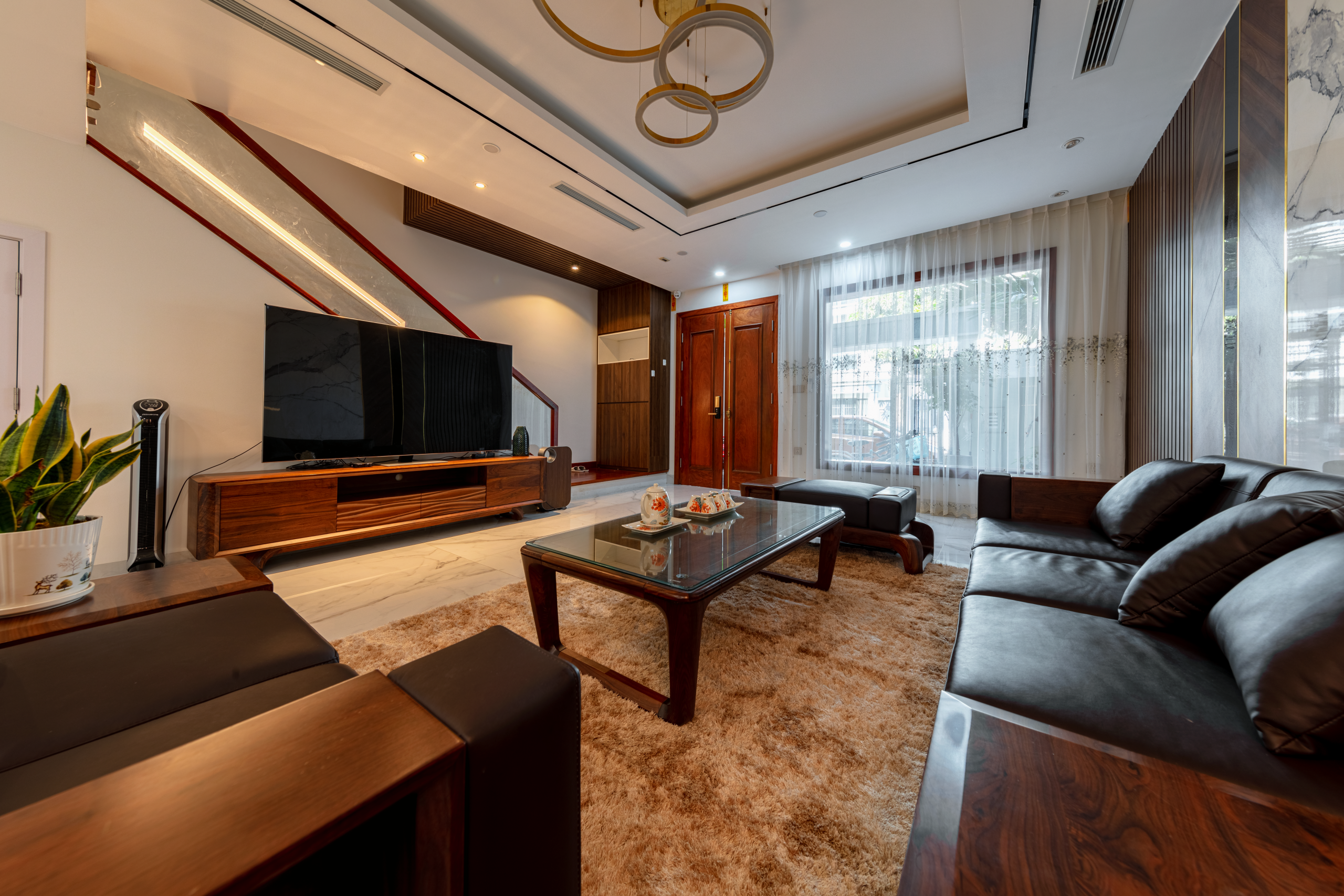 Phòng khách gây ấn tượng mạnh mẽ với bộ sofa da đen quyền lực kết hợp cùng bàn trà và kệ tivi làm từ gỗ óc chó tự nhiên
