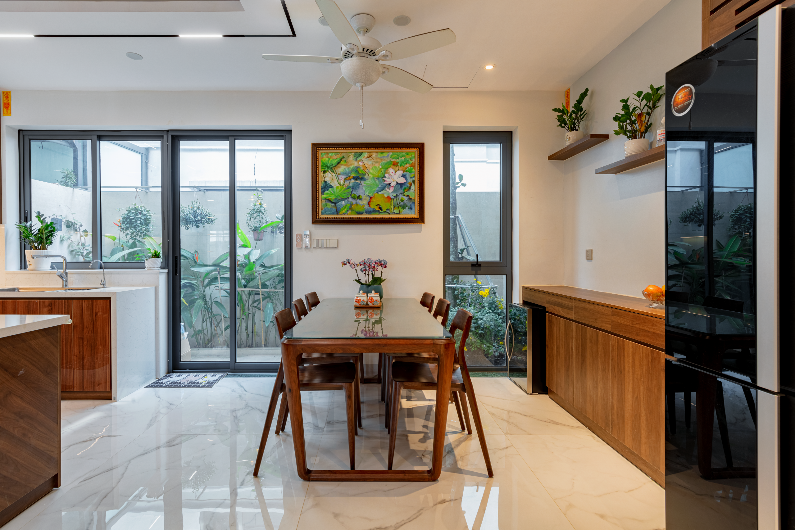 Bộ bàn ăn gỗ nguyên khối dành cho 6 người được đặt cạnh hệ cửa kính lớn nhìn ra sân vườn